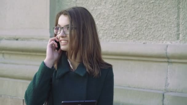 La chica hablando en el teléfono móvil, mirando a un lado en el fondo de la pared 4k — Vídeos de Stock