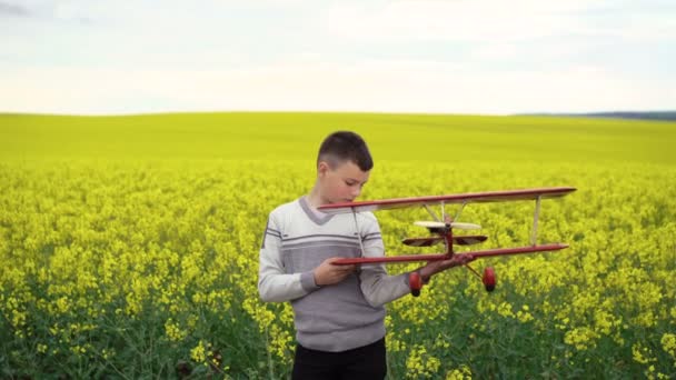 Knappe kind houdt zelfgemaakte vliegtuig op de canola-achtergrond. 4k — Stockvideo