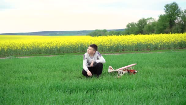 Rapaz com avião de brinquedo sentado em trigo verde. 4k — Vídeo de Stock