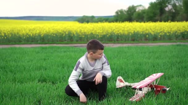 Lindo chico con helicóptero casero sentado en el trigo y mira al cielo. 4k — Vídeos de Stock