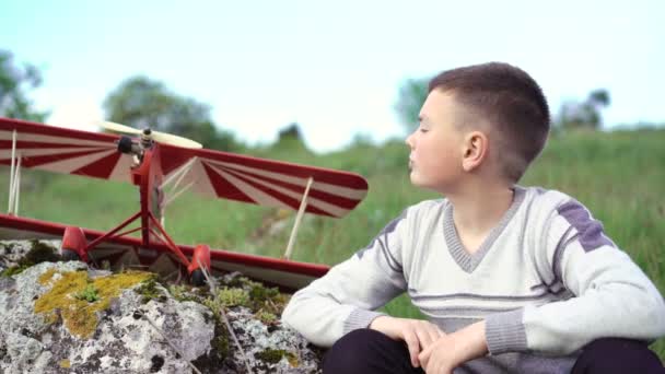 Close-up jongen zitten in de buurt van speelgoed vliegtuig op de steen en kijken op de hemel. 4k — Stockvideo