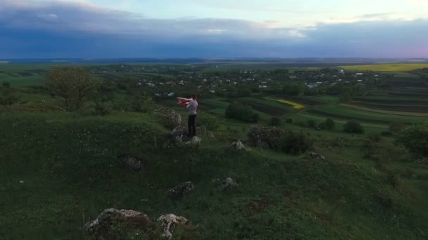 Kind houd speelgoed helikopter op een groene rots boven het dorp. Luchtfoto — Stockvideo