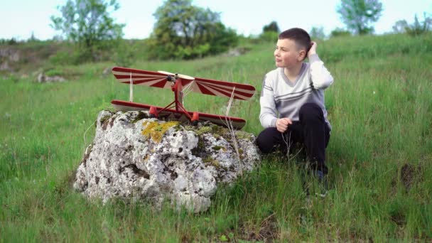 Νεαρό αγόρι κάθεται κοντά σε αεροπλάνο παιχνίδι στην πέτρα. 4k — Αρχείο Βίντεο