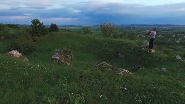 Child hold toy airplane on a green rock over the village. Aerial view — Stock Video