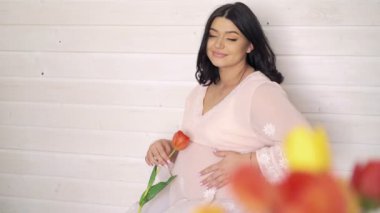 Bej renkli duvar, Lale tutarak önce mutlu parlak hamile oturma. 4k