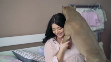 Hamile kadın bir yatakta evcil köpek ile oynarken. 4k