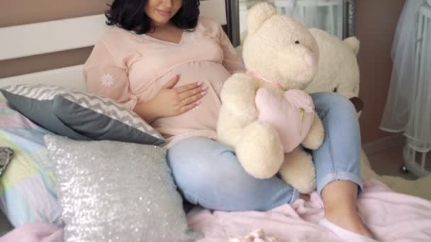Schwangere liegt mit Teddybär und streichelndem Bauch auf einem Bett. 4k — Stockvideo