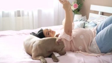 Hamile kadın ve evcil köpek yatakta yatarken ve selfie için poz. 4k