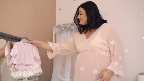 Kobieta w ciąży, patrząc na ubrania w pokoju przetargu przyszłość dziecka. 4k — Wideo stockowe