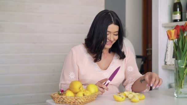 Mujer embarazada comiendo manzana sonriendo en la cocina cerca de los tulipanes. 4k — Vídeo de stock