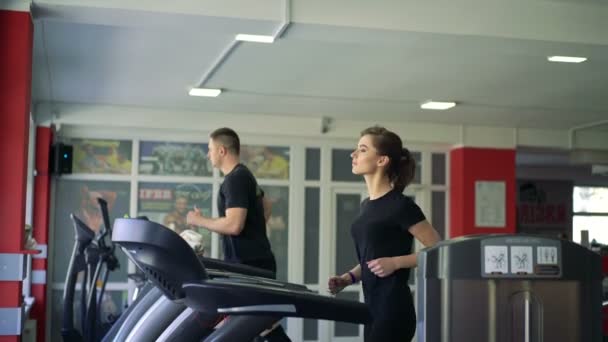 Um homem e uma rapariga a correr na passadeira do ginásio. 4k — Vídeo de Stock