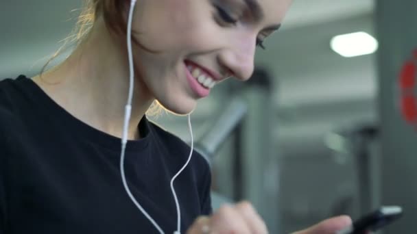 Jonge lachende vrouw op de sportschool luisteren naar muziek met behulp van een mobiele telefoon. — Stockvideo