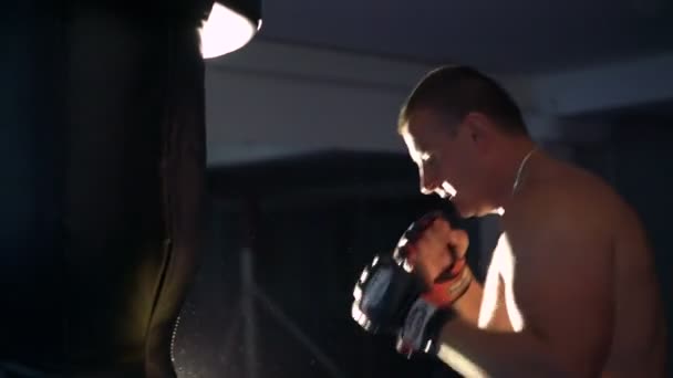 Stark pojke gör övning med slagsäck i mörka gymmet 4k — Stockvideo