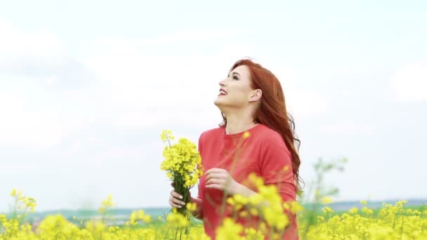 Mulher com flor de estupro no campo, vento a soprar. Movimento lento — Vídeo de Stock