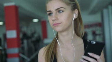 Güzel sarışın koşu bandı üzerinde telefon kullanır ve müzik. 4k