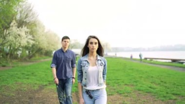 Güzel kız kamerada, arkasında bir deniz kenarında parkta çocuğa yürüyüş. 4k