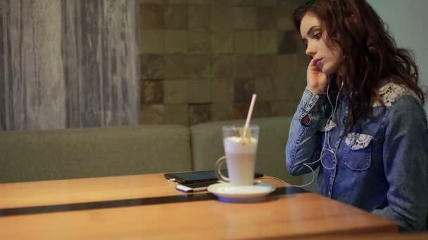 Привлекательная молодая женщина слушает музыку и пьет допоздна в кафе в городе — стоковое видео