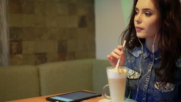 Mooi meisje luistert naar muziek in een café — Stockvideo