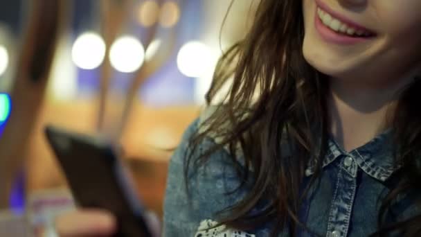 Wesoła dziewczyna przy użyciu telefonu, uśmiechając się w kawiarni. 4k — Wideo stockowe