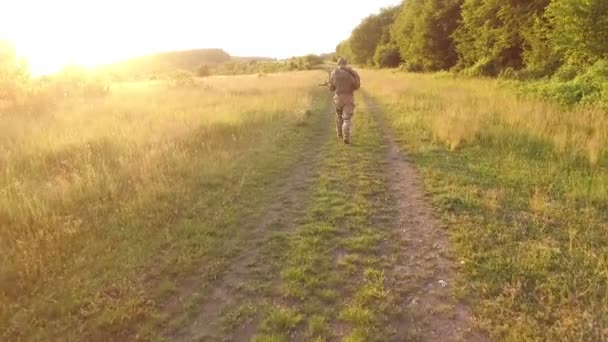 Vista aérea: Soldado va en camino en el campo. Cámara detrás de él — Vídeo de stock