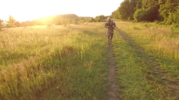 Вид с воздуха: Вооруженный солдат быстро выходит в поле на закате — стоковое видео