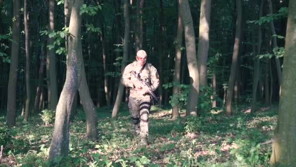 Fuerte militar va en el bosque con autómata y mira hacia atrás — Vídeos de Stock