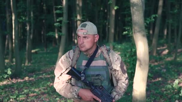 Bewaffneter junger Militär tritt in den Wald und blickt zurück. Zeitlupe — Stockvideo