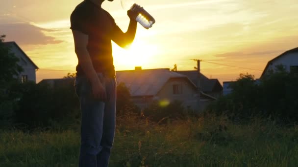 Hombre guapo bebiendo agua y luego vertiendo agua sobre la cabeza al atardecer. Despacio. — Vídeos de Stock