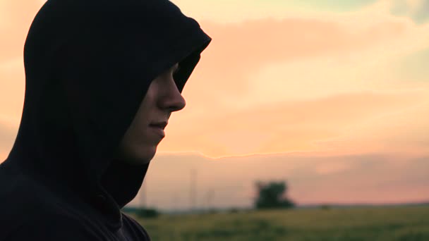 Profil des Mannes mit Kapuze auf dem Hintergrund des Sonnenuntergangs. Zeitlupe — Stockvideo