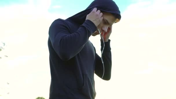 Молодой человек слушает музыку в наушниках на белом солнечном фоне неба — стоковое видео