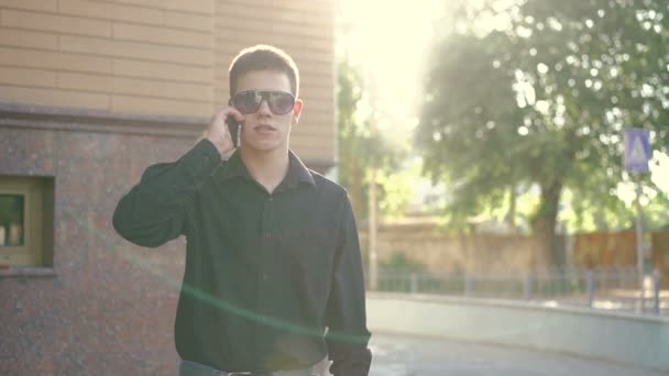 Модный бизнесмен говорит по телефону и курит электронную сигарету на улице — стоковое видео