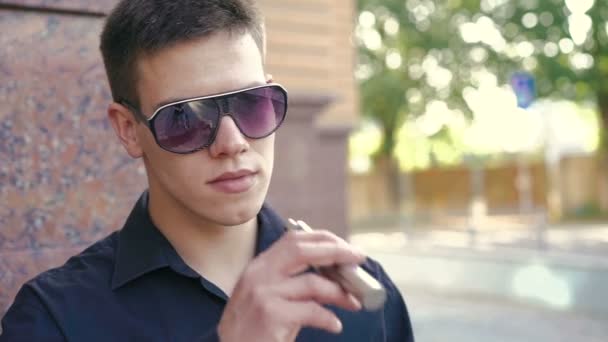 Portré a jóképű dohányzó e-cigaretta unwears napszemüveg és a szem villog — Stock videók