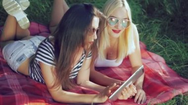 Battaniye çim üzerinde yalan ve tablet kullanarak iki kız. 4k