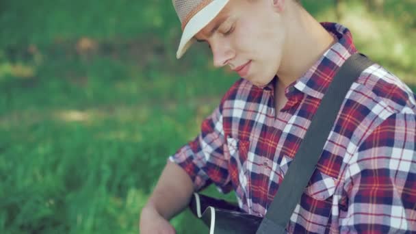 Portret van gitarist in hoed gitaarspelen in zonnige groen park. 4k — Stockvideo