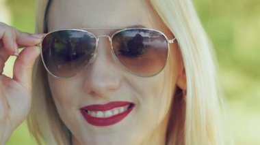Seksi sarışın bordo dudakları ile güneş gözlüğü alır. Yavaş yavaş