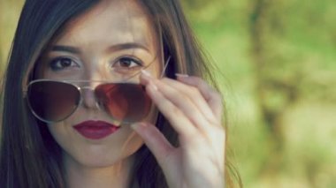 Seksi esmer bordo dudakları ile güneş gözlüğü alır ve kamera üzerinde görünüyor. Yavaş yavaş