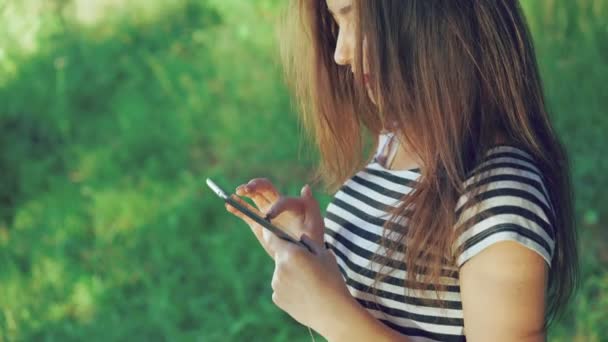 Una chica bonita usando el teléfono en el parque. 4k — Vídeos de Stock