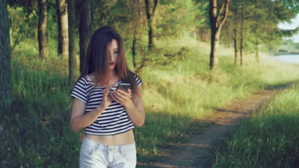 Νεαρό κορίτσι χρησιμοποιώντας smartphone εκτός στο υπόβαθρο φύση πράσινα δέντρα. 4k — Αρχείο Βίντεο
