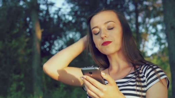 Menina de estilo olhando no telefone e tocando o cabelo no parque. 4k — Vídeo de Stock