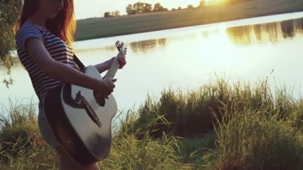 Holka hraje na kytaru večerní rybníka. 4k — Stock video