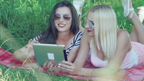 Filles avec une tablette à écran tactile couché sur l'herbe dans des lumières ensoleillées — Video
