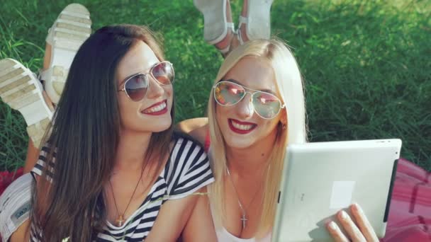 Mädchen mit einem Touchscreen-Tablet liegen im Gras in sonnigem Licht. langsam — Stockvideo