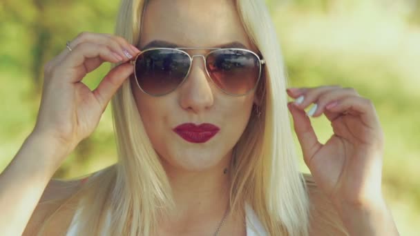 Σέξι ξανθιά συγκινητικό γυαλιά ηλίου στο παρασκήνιο φύση. Σιγά-σιγά — Αρχείο Βίντεο