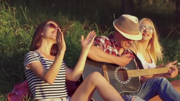 Twee meisje met grappige jongen met gitaar in het zonnige park vreugde. Slow motion — Stockvideo