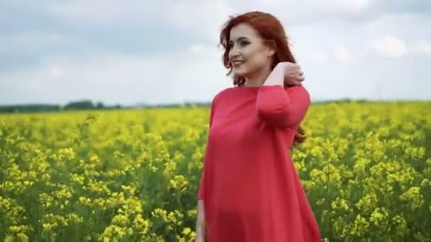 Jolie fille rouge debout avec un champ de colza en arrière-plan, souriant 4K — Video