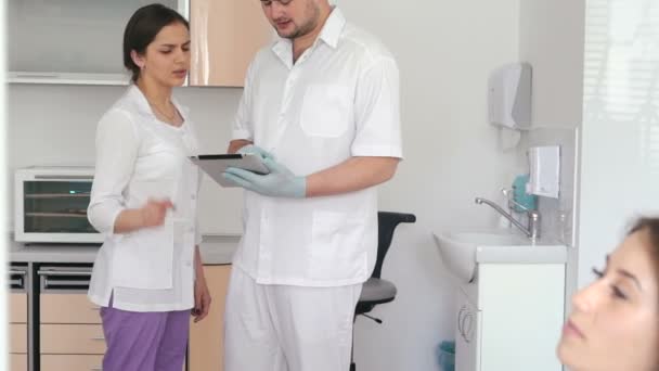 Dentista discutindo diagnóstico de sua paciente com jovem assistente — Vídeo de Stock