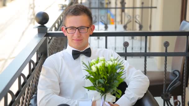 Junger Mann sitzt mit Hochzeitsstrauß auf dem Balkon und spricht — Stockvideo