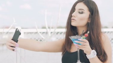 Genç kız sahilde kokteyl mavi kadehi ile selfie için poz. Yavaş yavaş