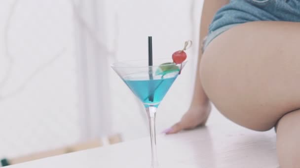 Close-up van goblet blauwe cocktail in de buurt van naakte dames benen — Stockvideo