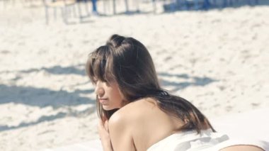 Kum üzerine yalan, saçlarını dönüm ve gülümseyen Bikini Beach kız. Yavaş yavaş